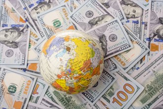 Model globe is placed on spread US dollar banknotes