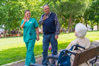 An elderly man with the nurse on a walk through the garden of a nursing home greeting an elderly woman