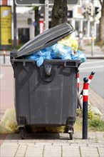 Filled rubbish container with open flap standing by the road