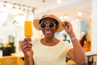 Black African ethnicity female customer eating a mango ice cream in a shop