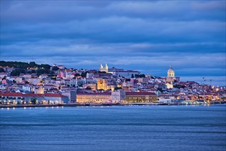 View of Lisbon over Tagus river with passing ferry boat from Almada with ferry in evening twilight. Lisbon