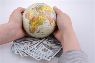 Human hand holding a model globe by the side of aAmerican dollar banknotes on white background