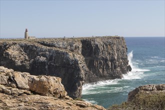 Surf on rocky cliffs in the Atlantic Ocean and the Farol de Sagres lighthouse on the site of the Fortaleza de Sagres fortress