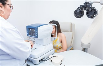 Specialist performing eye exam to female patient. Optometrist checking the eyesight of a patient with an autorefractor