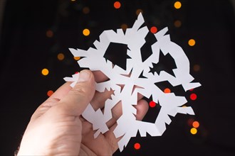 Snowflake shaped paper in hand on bokeh light background