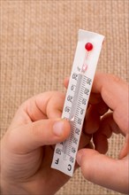 Hand holding a thermometer on a brown color background