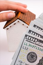 Human hand holding a model house by the side of aAmerican dollar banknotes on white background