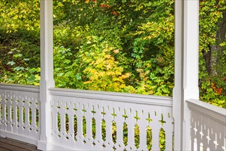 Railing on a veranda with wooden carpentry by a deciduous trees with autumn colors