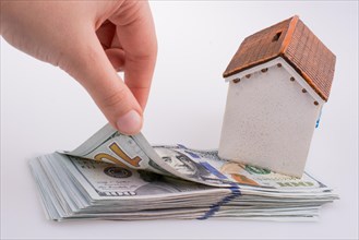 Human hand holding American dollar banknotes by the side of a model house on white background