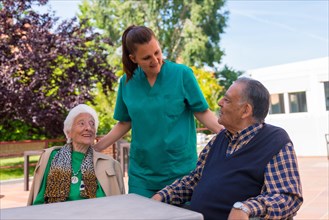 Two elderly people with the nurse in the garden of a nursing home or retirement home
