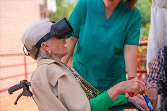 An elderly woman with the nurse looking through virtual reality glasses in the garden of a nursing home