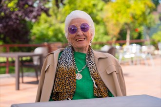 An elderly woman smiling in the garden of a nursing home or retirement home at a summer party wearing sunglasses