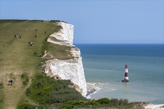 Tourists walking along the chalk cliffs overlooking Beachy Head lighthouse