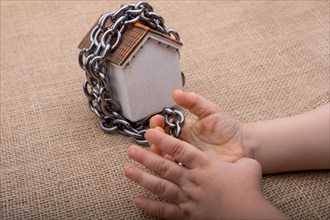 Little hand holding a chain around a model house on a brown background