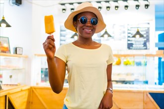 African black ethnicity woman eating a mango ice cream in a shop