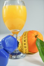 Orange with leaves surrounded by a tape measure with dumbbells and a glass of fresh orange juice