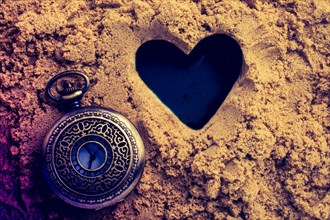 Retro style watch beside a heart shape made on sand
