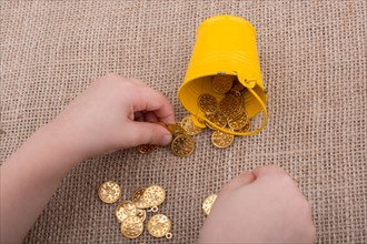 Bucket and fake gold coins in hand on canvas background