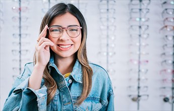 Portrait of beautiful girl modeling glasses in an optical store. Happy teen girl in eyeglasses with store eyeglasses background
