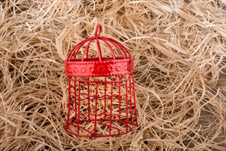 Red color bird cage placed on a straw background