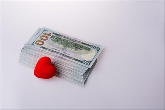 American dollar banknotes by the side of a red color heart shaped object on white background