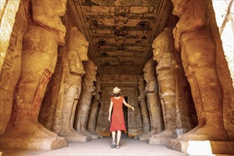 A young woman in a red dress at the Abu Simbel Temple next to the sculptures