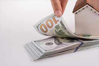 Human hand holding American dollar banknotes by the side of a model house on white background
