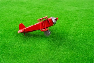 Red little retro model airplane in green grass