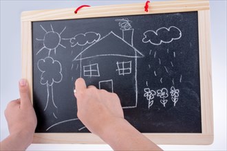 Hand drawing a house on the blackboard with a chalk