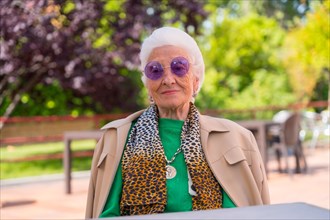 An elderly woman in the garden of a nursing home or retirement home at a summer party wearing sunglasses