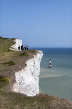 Tourists on the edge of the chalk cliffs overlooking Beachy Head lighthouse