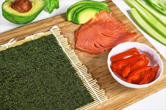 Preparing homemade sushi with blank Nori algea sheet on bamboo mat and ingredients like smoked salmon and tomatoes
