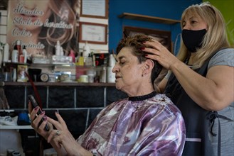 Latin hairdresser salon. Client checking her cell phone and hairdresser massaging her hair. General shot