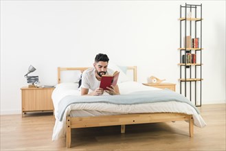 Man lying bed reading book bedroom