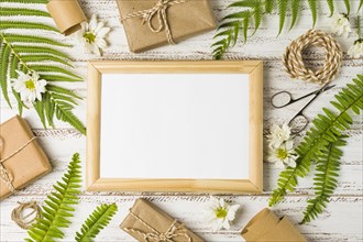 Elevated view blank frame surrounded by gifts leaves white flowers