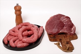 Fresh homemade sausages on a black plate and beef tenderloin on a wooden board isolated on a white background