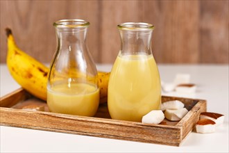 Two drinking jars with yellow banana and coconut smoothies on wooden tablet