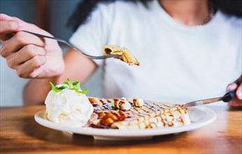Close up of woman eating chocolate crepe and ice cream with fork. Hands of person with fork cutting chocolate crepe and ice cream