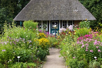 Farm garden with thatched pavilion and colourful variety of flowering summer flowers and perennials