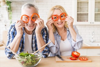 Smiling portrait senior couple looking through red bell pepper slice