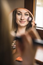 Reflection smiling woman applying blusher her face
