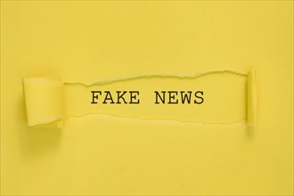 Torn fake news paper yellow wall