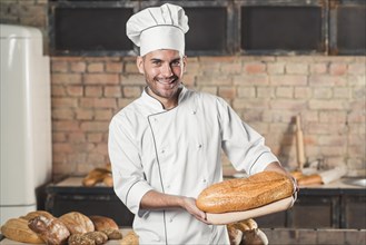 Smiling male baker holding baked bread chopping board