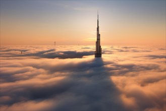 Burj Khalifa building in Dubai above the sea of clouds at sunrise