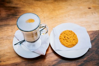 Delicious hot cappuccino coffee with cookie on wooden background. Cup of cappuccino with cookie on wooden table
