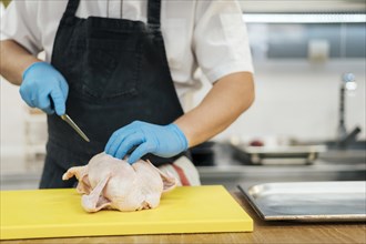 Front view chef with gloves cutting chicken