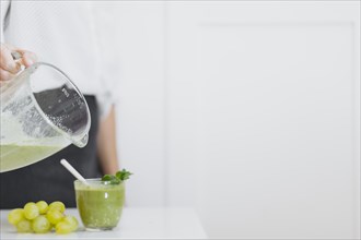 Crop person pouring green smoothie glass