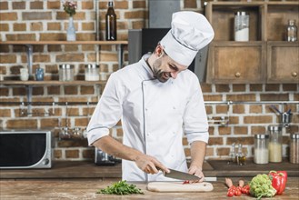 Happy young male chef cutting red chili with knife kitchen counter