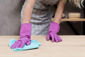 Midsection female janitor wiping wooden table with cloth