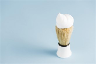 Overhead view classic shaving brush with white foam against blue background